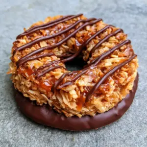 A single No-Bake Samoa Cookie held up, showing the dense toasted coconut flakes and glossy dark chocolate bottom. (No-Bake Samoa Cookies)