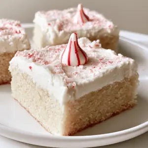 Close-up handheld photo of square Peppermint Sugar Cookie Bars on a white plate.