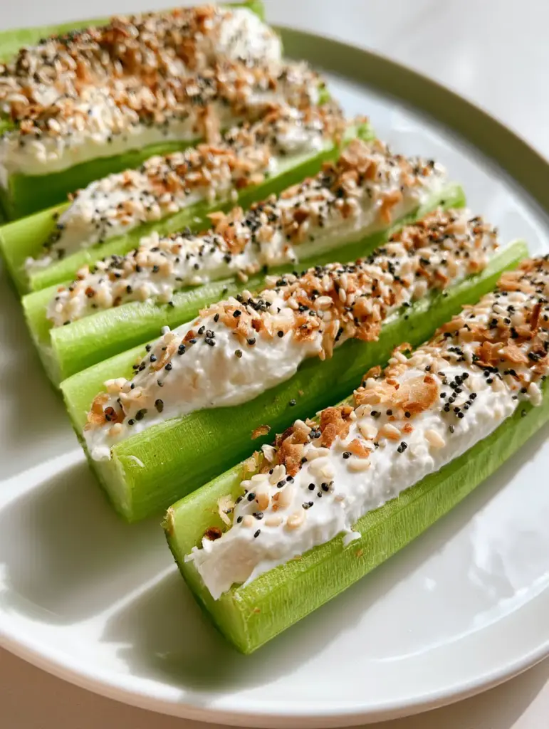 Close-up of fresh raw celery stalks filled to the brim with smooth cream cheese and garnished with sesame and poppy seeds.