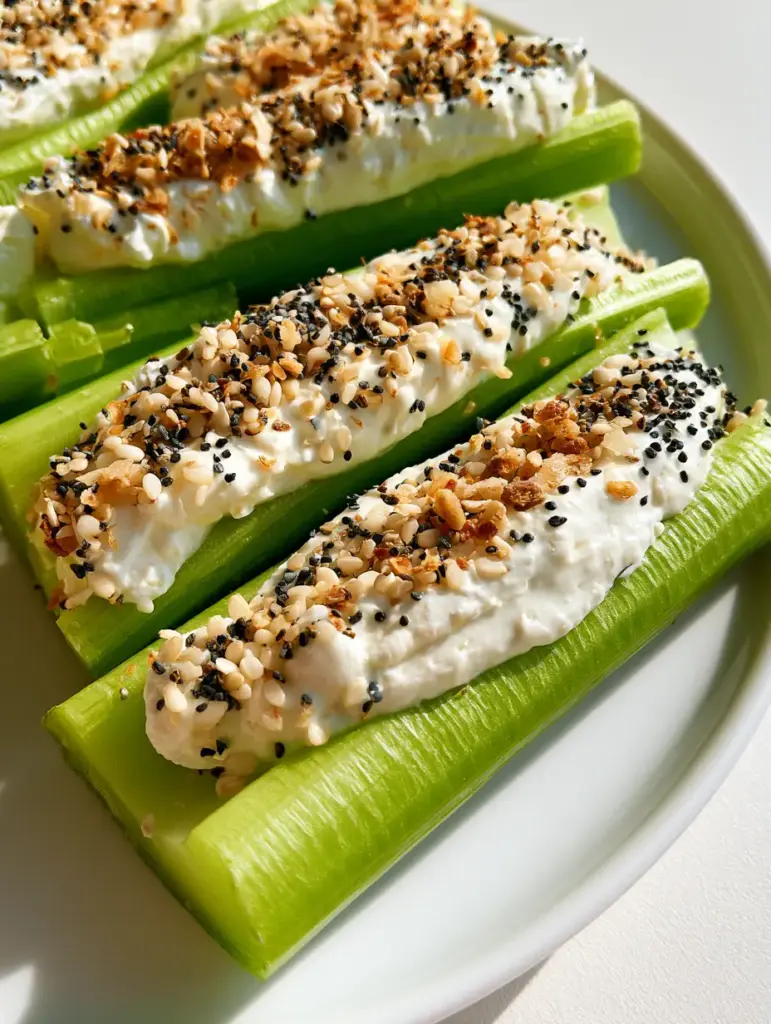 Stuffed Celery with Everything Seasoning and Creamy Filling 1 Symmetrical arrangement of stuffed celery on a white plate showing the heavy garnish of dried garlic and onion flakes.