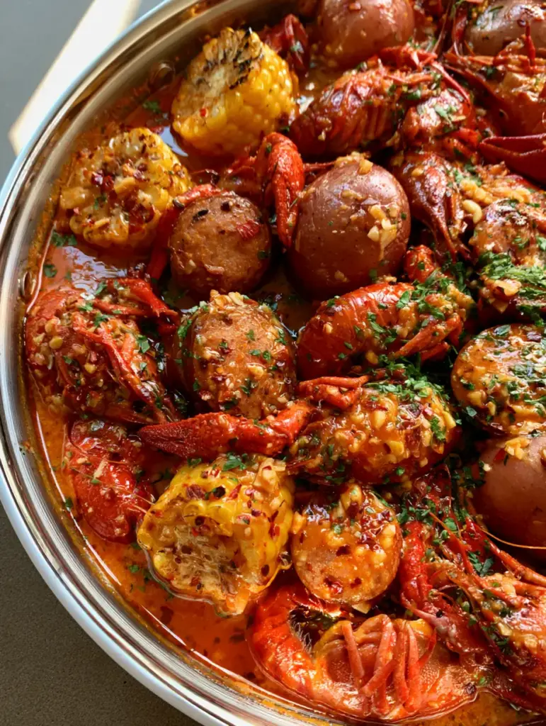 Home 6 Top-down view of a silver pot with crawfish, charred corn, and sausage in a thick Seafood Boil Butter Sauce.