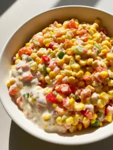 Close-up of Creamy Corn Salad featuring sweet corn kernels, diced peppers, and celery in a thick white dressing. (Creamy Corn Salad)